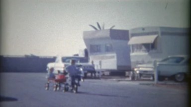 1962: Kid riding bike pulling wagon around mobile trailer home park.