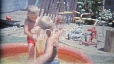 1963: Brother Intimidating Sibling With Bucket of Water in Summer Play