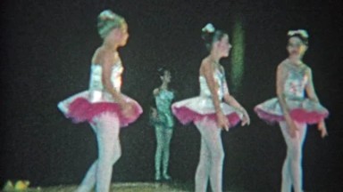 1963: Ballet troupe young girls dancing on black background grade school stage.