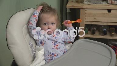 Mom feeding baby cheese on a high chair from a spork utensil.