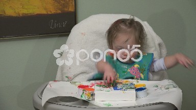 Messy baby finger painting closeup with paint on forehead and everywhere.