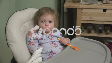 Baby girl being fed yogurt and reaching high for the sky.