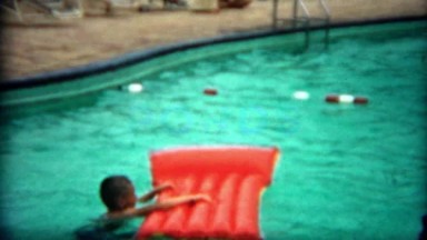1955: Boy Paddling on Swimming Raft Around Hotel Pool