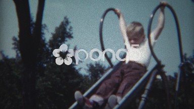 1954: Kid brothers going down high metal slide at urban city park.
