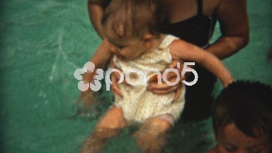 1954: Mother teaching baby to swim at the pool while distracted.