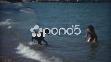 1954: Women playing with large black dog on windy beach.