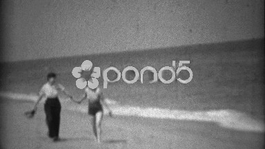 1936: Sisters walking together on beach in swimwear fashion and high pants.