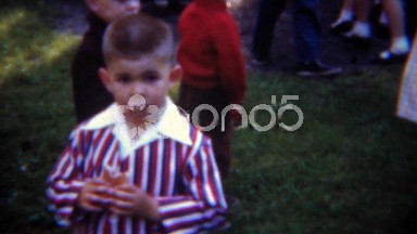 1953: 4th of July party boy dressed in patriotic stripes eating hotdog.