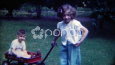 1953: Young Girl Pulling Toddler Boy in Red Wagon Around Front Yard, Erie, Pennsylvania