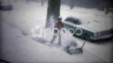 1967: Man using snowblower machine after winter storm on urban sidewalk.