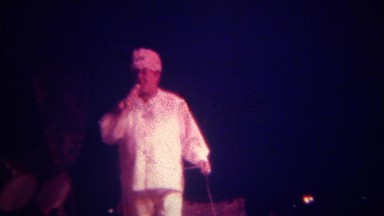 1973: Wacky big man emcee host with microphone dressed in white costume.