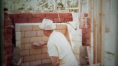 1966: Brick fireplace construction worker brushing stones clean preparing