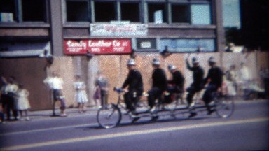 1964: Old timey police officer riding 5 person bike at parade. BUFFALO, NEW YORK