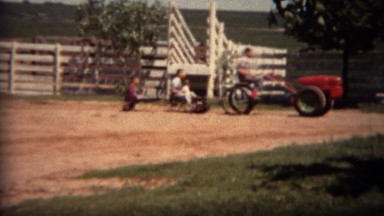 1951: Odd farm riding lawnmower pulling train of children in wagons. LINCOLN,
