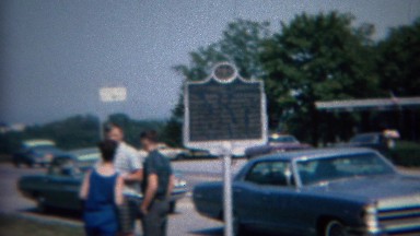 1968: Family outdoor deciding at classic parked cars and historic sign.