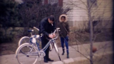 1971: African Girl Jokes with Caucasian Man Fixing Bicycle in Driveway