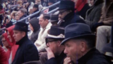 1971: Multicultural fedora hat wearing men in sports stadium crowd.