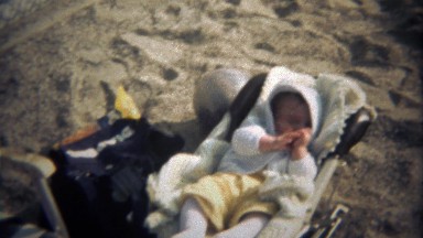 1979: Baby in Carrier Falling Asleep Sucking Thumb on Beach Sand.