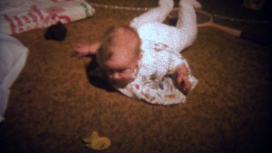 1979: Newborn baby girl practicing tummy time exercises on carpet.