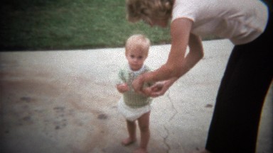 1979: Caucasian blonde toddler pulling school bus toy on sidewalk.