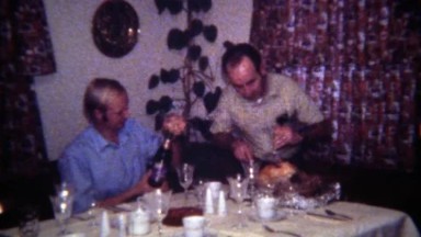 1971: Gay men couple carving turkey pouring wine for holiday celebration.