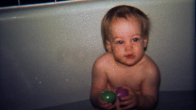 1974: Baby boy smiles playing in bathtub with plastic toys.
