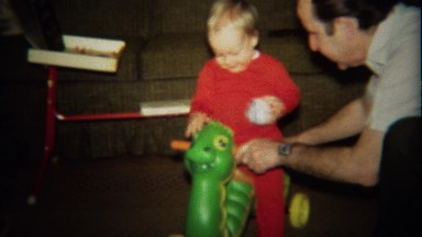 1974: Grandpa plays with baby on turtle toy scooter.