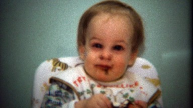1974: Baby getting messy eating big chocolate candy treat.