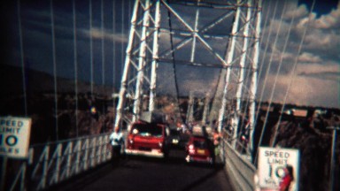 1972: Car crossing narrow suspension bridge on a windy day.