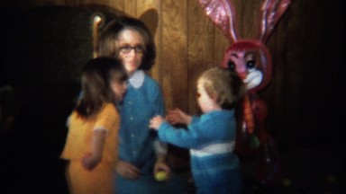 1974: Vintage mom plays with kids at Easter with doll in background.