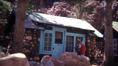 1972: Man entering small rural cabin with hiking backpack on.