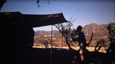 1972: Man setting up camping tent silhouette with beautiful mountain background.