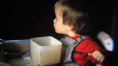 1971: Toddler boy eats cereal from square tupperware bowl.