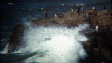 1971: Wave crashes on rocky shoreline almost hitting bystanders.