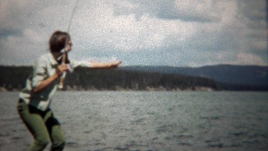 1971: Teenage girl catches trout fish in mountain lake setting.