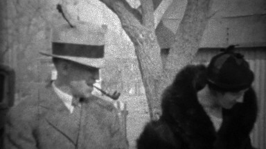 1933: Man smoking pipe wife in black fur coat with funny formal hats.