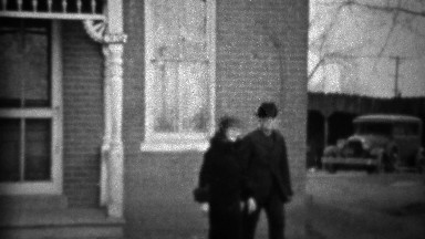 1933: Grandparents walking front yard dressed in black clothes.