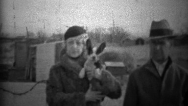1933: Couple showing off new small dog in formal winter clothing.