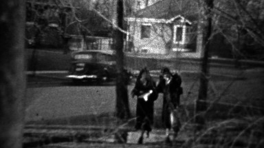 1933: Women on neighborhood sidewalk past classic model A car.