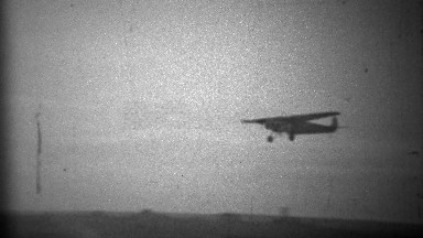 1934: Propeller plane landing in primitive airport landing strip.