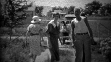 1934: Family skipping towards camera in front of Ford model A car.