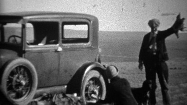 1934: Man holding up hunted dead bird beside model A car.