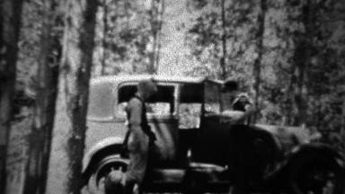1934: Couple packing Ford model A car in deep wooded forest.