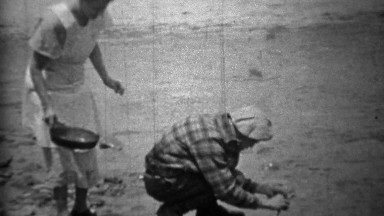 1935: Man cleaning fish creekside while wife brings frying pan.