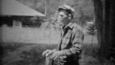 1935: Man smoking pipe proudly holding up freshly caught trout fish.
