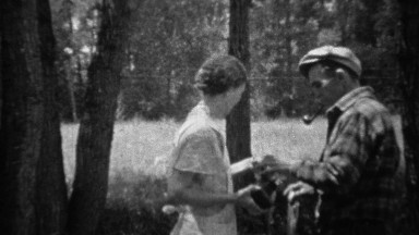 1935: Man photographs woman holding up recently caught trout fish.