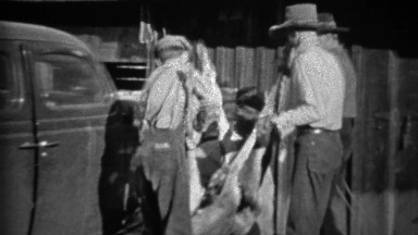 1935: Men tie dead hunted deer to front of Plymouth car for transport.