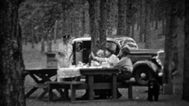 1935: Family picnic in pine tree forest at new black Plymouth car.