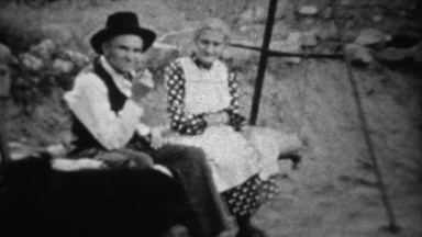 1939: Grandparents rocking on porch swing with black dog.