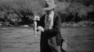 1939: Fisherman Wading in Fast Stream Showing Trout Catch